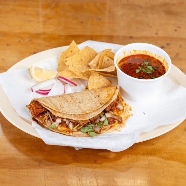 Birria taco with onions and cilantro, tortilla chips, lemon, radishes, and a cup of consommé.