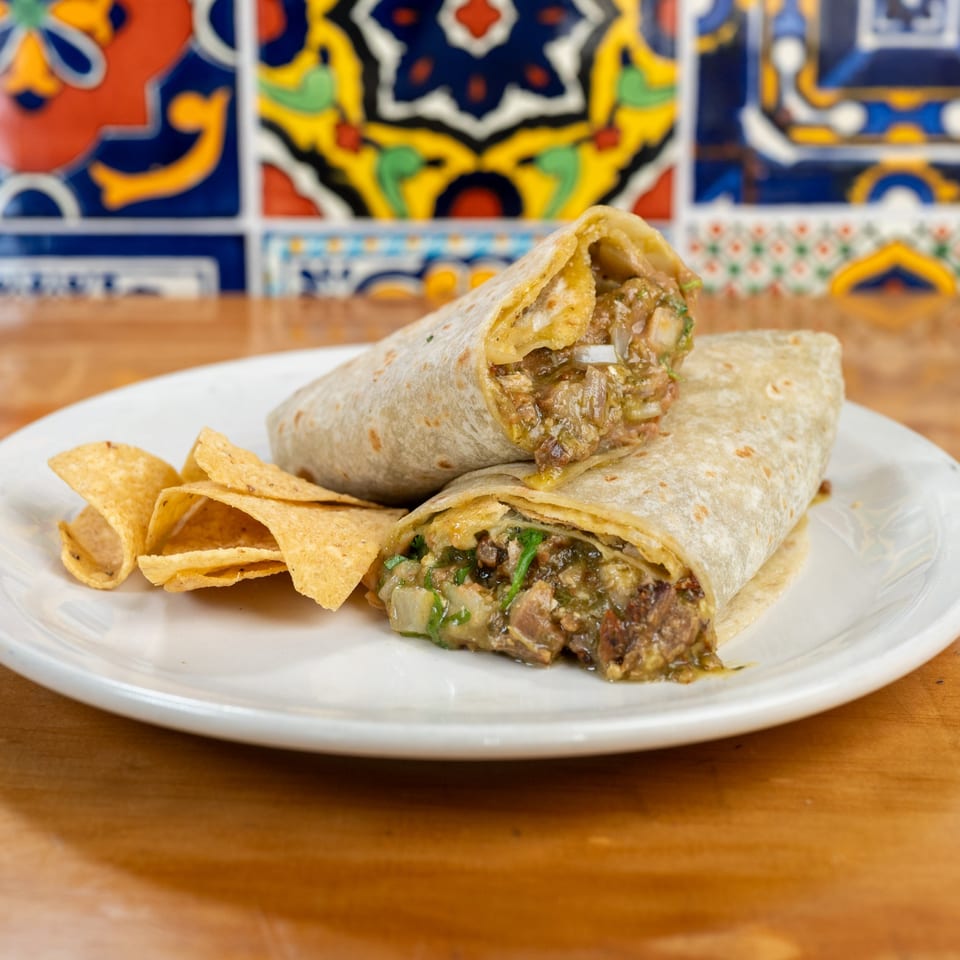 Two burritos filled with meat and green salsa, served with tortilla chips on a white plate.