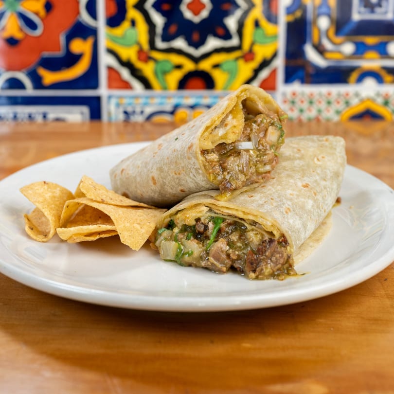 Two burritos filled with meat and green salsa, served with tortilla chips on a white plate.