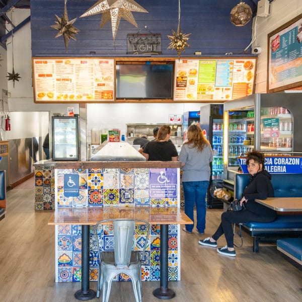 Inside Cotijas Taco Shop, customers order at the counter with menus above, and a woman sits at a booth.