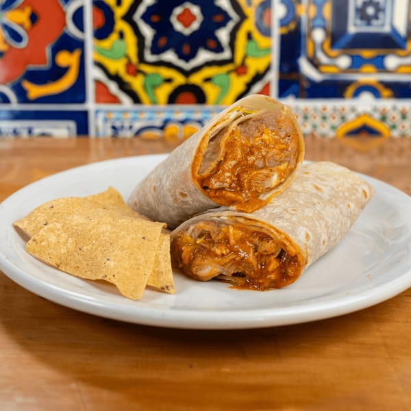 Two burritos, one cut open, filled with meat and sauce, served with tortilla chips on a white plate.