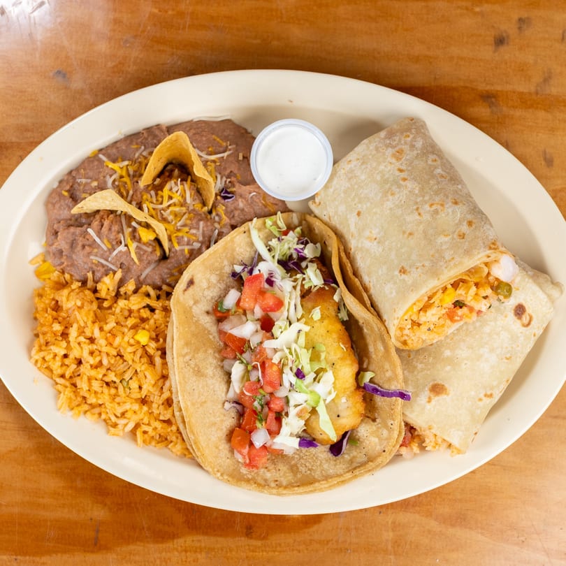A plate of Mexican food with a fish taco, burrito, refried beans, rice, and a side of sauce.