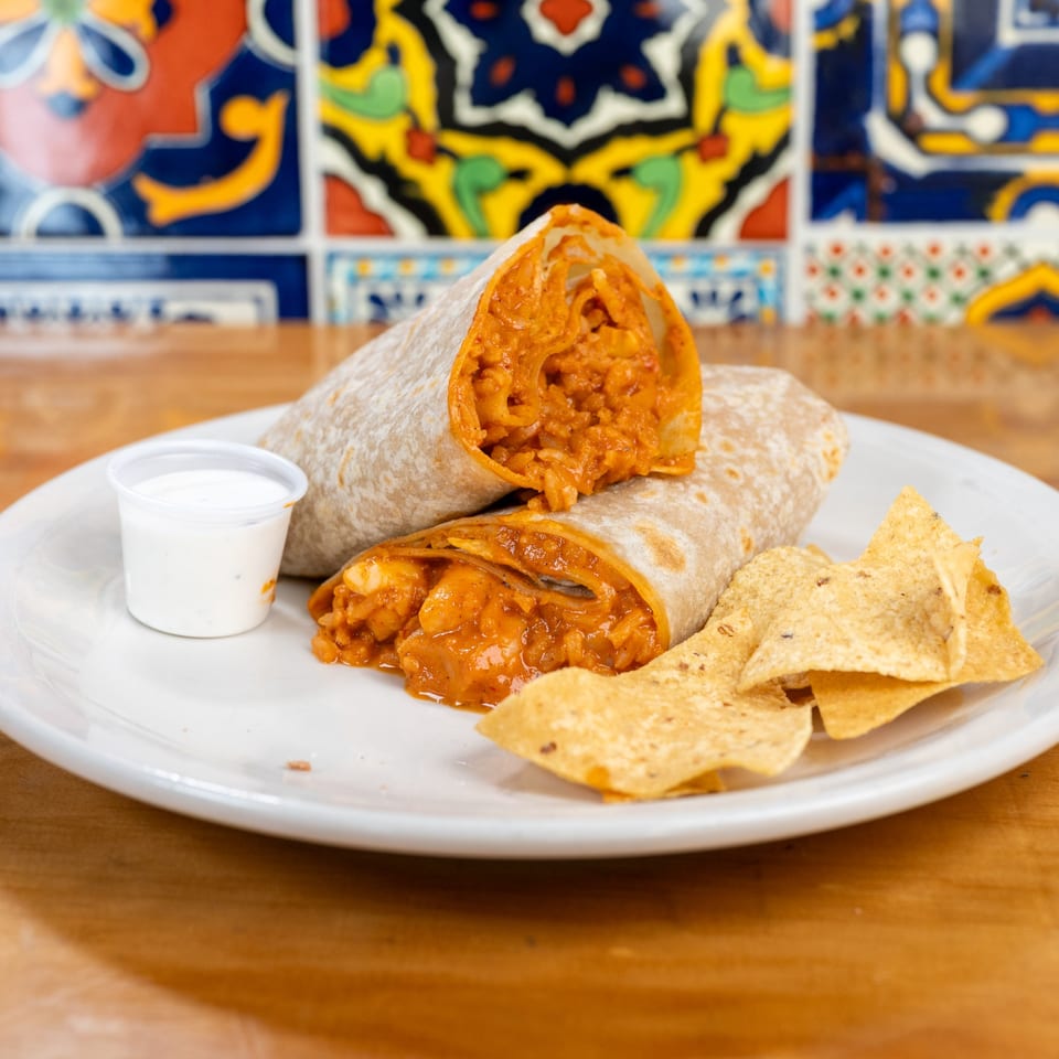 Two burritos cut in half, revealing a savory orange filling, served with tortilla chips and a side of white sauce.