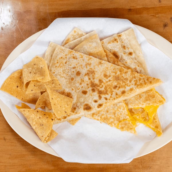 A plate of golden-brown quesadilla triangles with melted cheese and a side of tortilla chips.