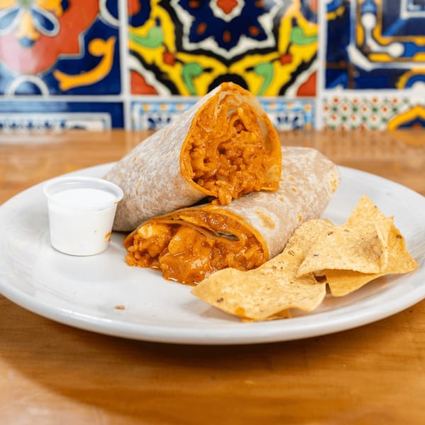 Two burritos cut in half, revealing a savory filling, served with tortilla chips and a side of sauce.